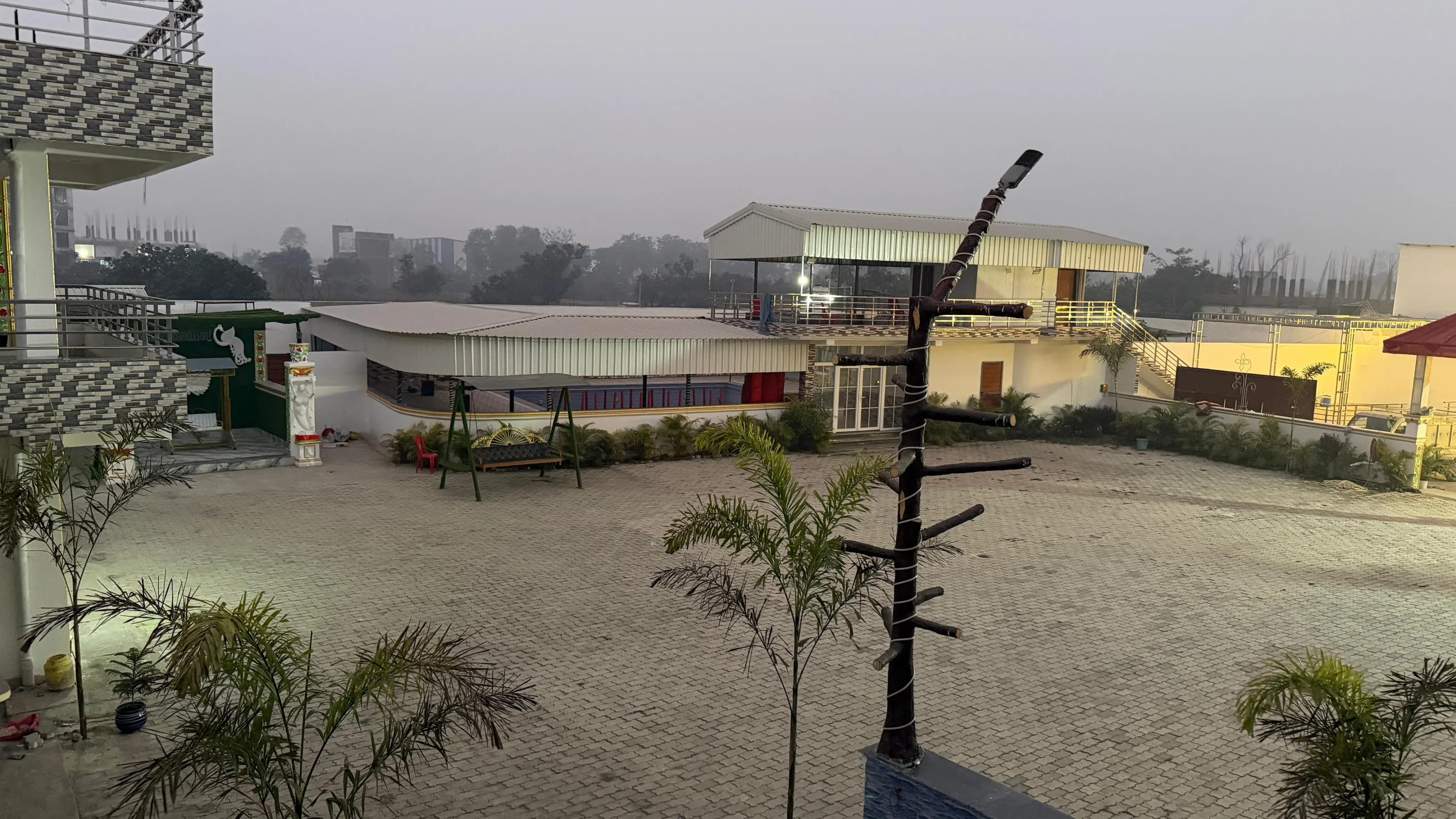 Elevated view across the Janki Resort grounds — the paved courtyard, the covered pool pavilion and the surrounding buildings at dawn